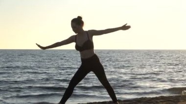 Sakin denizin yanındaki sahilde yoga yapan beyaz bir kadın, gündoğumu geçmişi var..