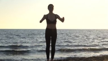 Sakin denizin yanındaki sahilde yoga yapan beyaz bir kadın, gündoğumu geçmişi var..