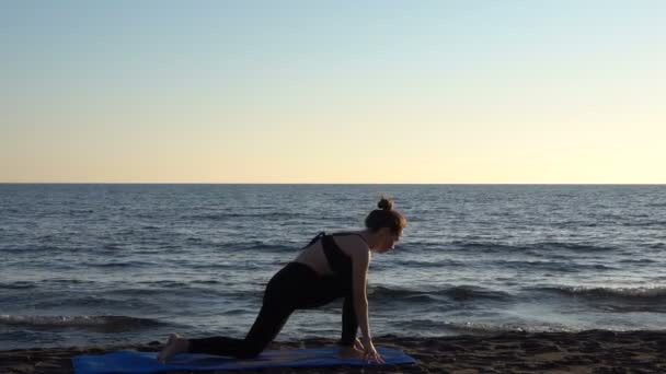 Sakin denizin yanındaki sahilde yoga yapan beyaz bir kadın, gündoğumu geçmişi var.. — Stok video