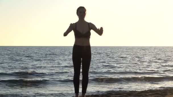 Junge kaukasische Frau praktiziert Yoga am Strand in der Nähe ruhigen Meeres, Sonnenaufgang Hintergrund. — Stockvideo
