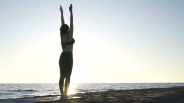 Genç beyaz kadın sakin denizin yanındaki sahilde yoga yapıyor..