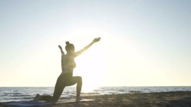 Genç beyaz kadın sakin denizin yanındaki sahilde yoga yapıyor..