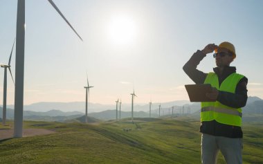 Rüzgar Türbinindeki Teknisyen Güç Üretici İstasyonu elinde bir tabletle ayakta duruyor.