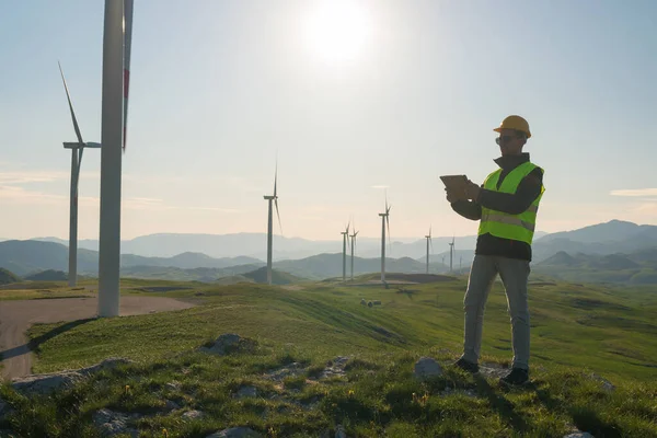 Technicien Ingénieur en éolienne Centrale électrique debout avec une tablette dans ses mains Image En Vente