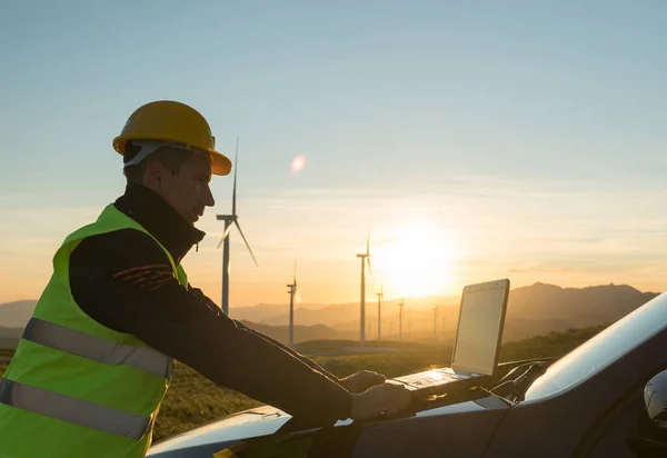 Ingeniero técnico en la estación de generación de energía de aerogeneradores comprueba el estado de las turbinas con un ordenador portátil Imagen de stock