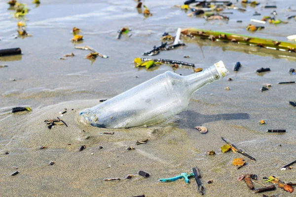 Glass water bottle pollution in the ocean (Environment concept). Ocean pollution: waste on the beach.