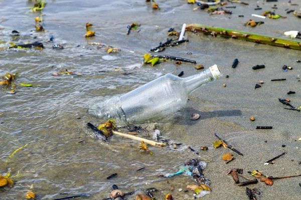 Glass water bottle pollution in the ocean (Environment concept). Ocean pollution: waste on the beach.