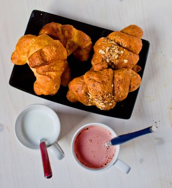 bir fincan süt ve çilekli siyah tepsi ve ağartılmış ahşap masa ile tahıl ve tereyağı kruvasan ile mükemmel sağlıklı kahvaltı