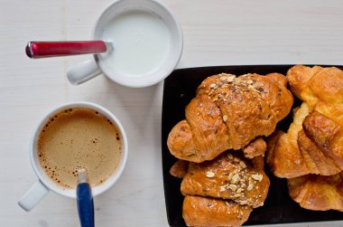 Mısır gevreği ve tereyağı kruvasan siyah tepsi ve bir fincan kapuçino ağartılmış ahşap masa ile mükemmel sağlıklı kahvaltı