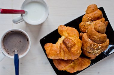 Mısır gevreği ve tereyağı kruvasan siyah tepsi ve bir fincan kahve ile ağartılmış ahşap masa ile mükemmel sağlıklı kahvaltı