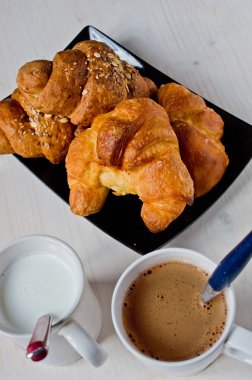 Tereyağı ve mısır gevreği ile mükemmel sağlıklı kahvaltı siyah tepside kruvasan ve ağarmış ahşap masa ile bir fincan süt ve çikolata.