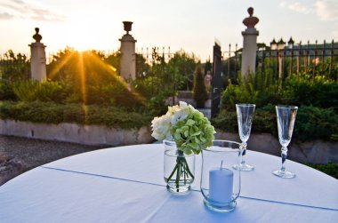 bouquet of white roses and hydrangeas and two glasses ready for lovers illuminated by the warm light of sunset clipart