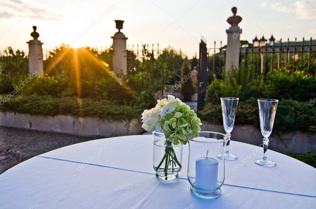 bouquet of white roses and hydrangeas and two glasses ready for lovers illuminated by the warm light of sunset