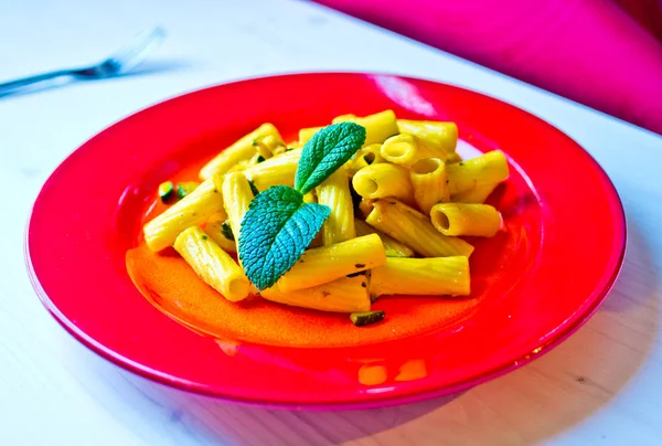 pasta dish topped with a bright yellow colored sauce with vegetables, saffron and tasty herbs