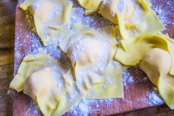 Italian housewife prepares egg pasta, stuffed tortelli on a pastry board, ready for the party lunch.