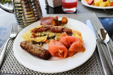 Bu beş yıldızlı bir otelde kahvaltı. Somon, sosis, yumurta omleti masanın üstünde. Çatal, bıçak ve kaşık, sürahi ve bir bardak domates suyu, Aruba, Ağustos 2014