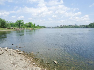 Mavi su ve mavi gökyüzü. Rocky Nehri kıyısı, arka planda yeşil ağaçlar ve binalar. Ottawa, Kanada 'daki merkez köprü.