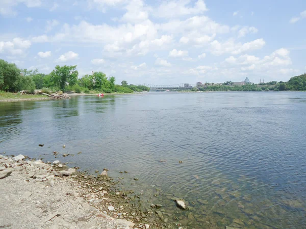 Mavi su ve mavi gökyüzü. Rocky Nehri kıyısı, arka planda yeşil ağaçlar ve binalar. Ottawa, Kanada 'daki merkez köprü.