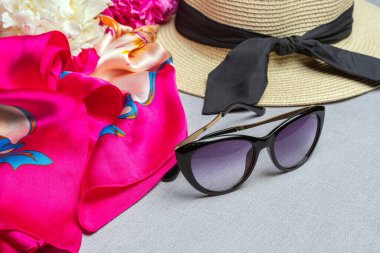 Güneş gözlüğü, hasır şapka, fuşya ipek fular, leylak arka planda beyaz ve pembe şakayıklar. Yaklaş, düz yat.  