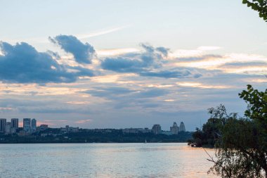 Şehir manzaralı. Gün batımında nehir. Bulutları olan renkli bir gökyüzü. Şehir manzarası, arkaplan