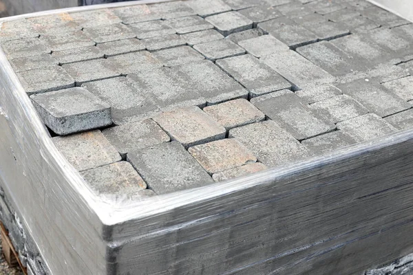 Pile of new grey paving stones on wooden pallet fixed with stretch wrap. Blocks texture, background, close-up