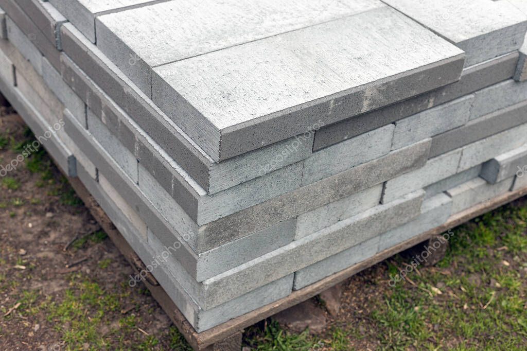 Pile of new and grey driveway or path edgings on wooden pallet on a construction site. 