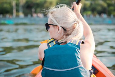 Sarışın genç bir kadın güneşli bir yaz gününde gözlerini kaçırıp nehirde kayak yapıyor. Kano yapmak için güzel bir zaman. Yaklaş, arka plan
