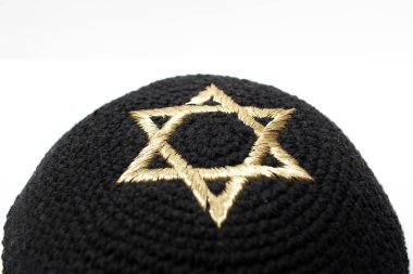 Beyaz arka planda altın renkli bir David yıldızıyla siyah bir kippah 'ın yakın çekimi..