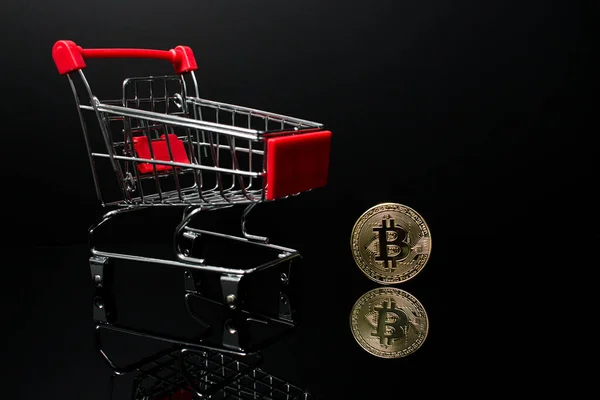Yanında kripto para birimi Bitcoin olan siyah arka planlı bir alışveriş arabası..