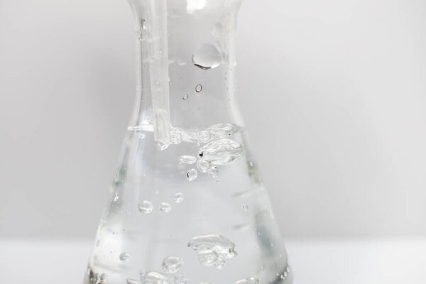 Closeup of a glass Erlenmeyer flask with a plastic pipette in it with bubbles in the liquid on a white background. Science.