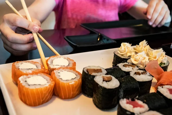 A set of sushi rolls on a table in a restaurant. Japanese food restaurant, sushi maki roll plate, platter set. Hand take roll.