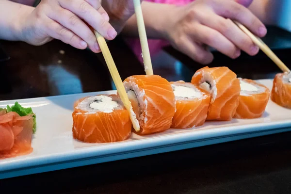 Eating Sushi with chopsticks. California Sushi roll set with salmon. Soft focus.