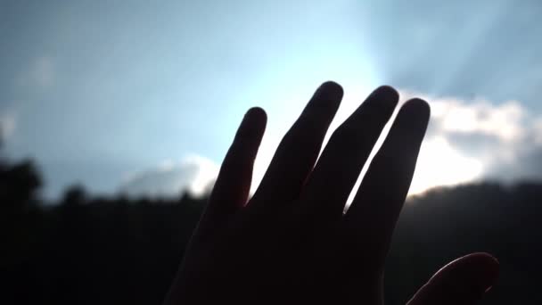 Ręka w sylwetce wzniesiona ku słońcu w górach podczas wschodu słońca z rozbłyskiem słońca przez palce — Wideo stockowe