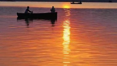 Güneşin doğuşu sırasında Varanasi 'deki kutsal nehir kenevirini geçen teknenin güzel sinematik görüntüsü suyu altın gibi parlatıyor.