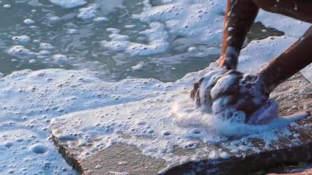 Руки стирают одежду на плоской скале в Варанаси, Индия с мыльными пузырями, текущими в воде реки Ганга, вызывая загрязнение воды - крупным планом — стоковое видео