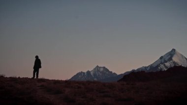 Uzakta duran bir adamın silueti, Spiti Vadisi 'ndeki dağlarla çevrili. 