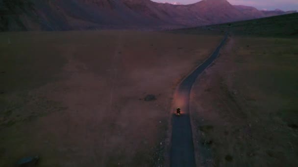 ヒマカル・プラデーシュ州スピティのヘッドライトが付いている暗闇の中で真っ直ぐなヒマラヤの道を行く自転車の空中安定ショット — ストック動画