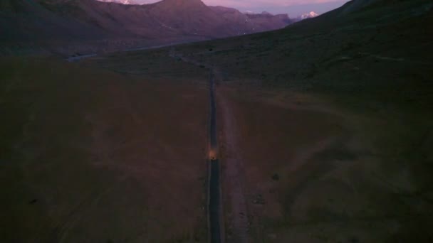 Luchtfoto na schot van een fiets gaan op een rechte himalaya weg in het donker met koplampen aan in Spiti, Himachal Pradesh — Stockvideo