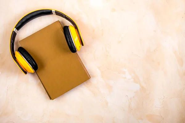 Book and yellow headphones on. Beige background top view copy space