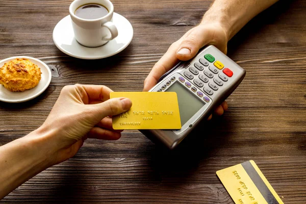 Payment transactions. Hand hold card near terminal on wooden cafe table