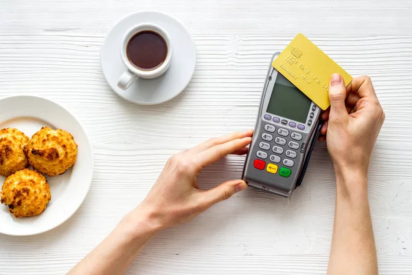 Payment transactions. Hand hold card near terminal on white cafe table top-down