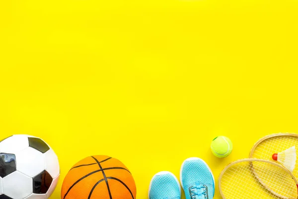 Sport games equipment - balls, sneakers, rockets - on yellow top view copy space