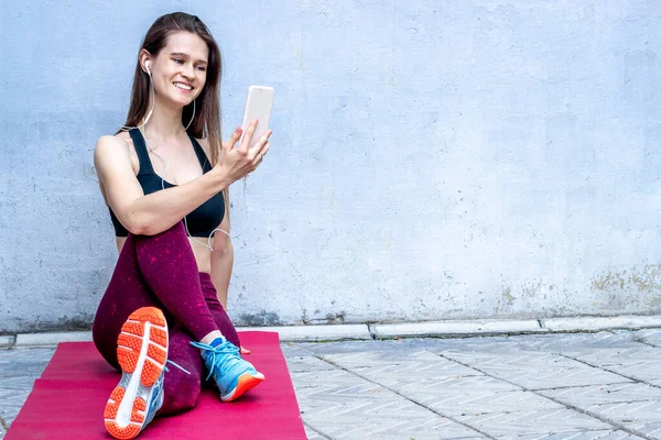 Sport woman talking on mobile phone stretching after training and smiling