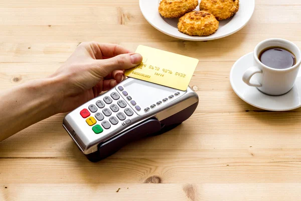 Payment transactions. Hand hold card near terminal on wooden cafe table