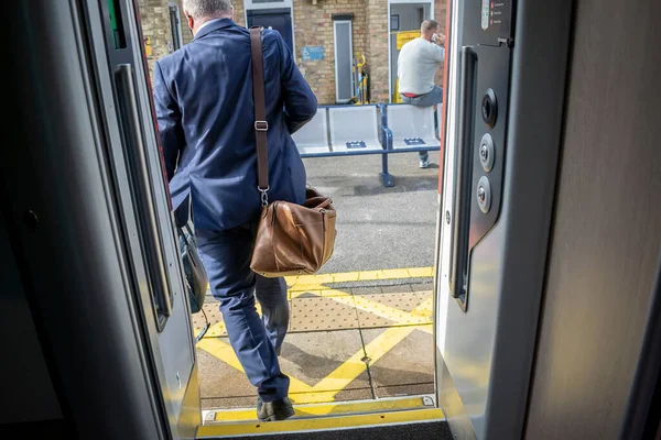 Businessman in blue suit and brown leather shoulder bag walking out of the train door.