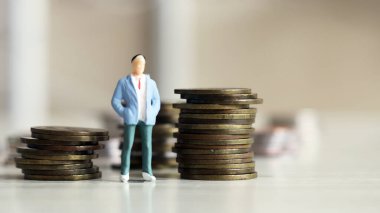 Bozuk para yığınının yanında duran minyatür bir adam..