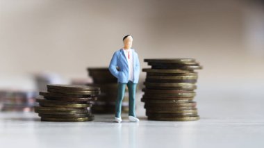 Minyatür ve bozuk para konsepti. Bozuk para yığınının yanında duran bir adam.