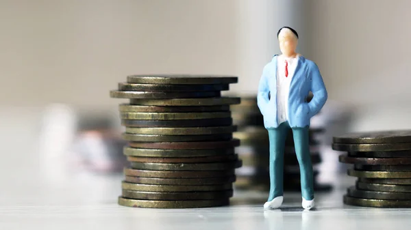 Concept of savings plan. A miniature man standing next to a pile of coins.