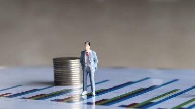 Minyatür İnsanlar ve Paralar. Çizelgedeki bozuk para yığınının yanında duran takım elbiseli adam..