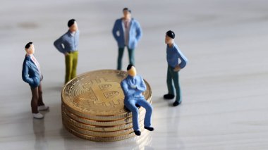 Bitcoin yığınıyla çevrili dört minyatür adam ve madeni paranın üzerinde oturan minyatür bir adam..